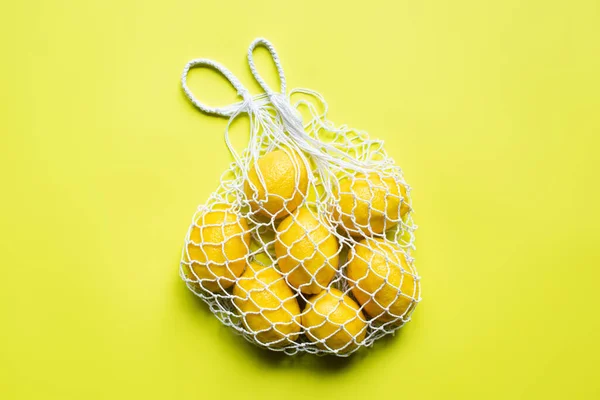 Top view of ripe whole lemons in string bag on yellow background — Stock Photo