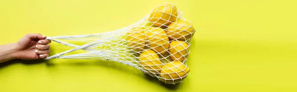 Vista cortada de mulher segurando limões inteiros maduros em saco de cordas no fundo amarelo — Fotografia de Stock