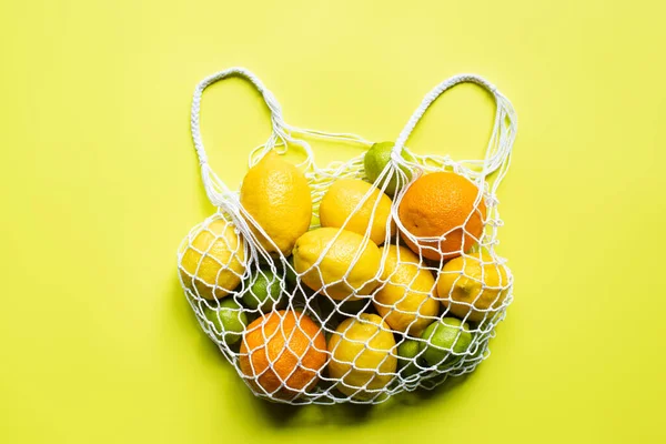 Vista superior de frutas cítricas inteiras maduras em saco de cordas no fundo amarelo — Fotografia de Stock