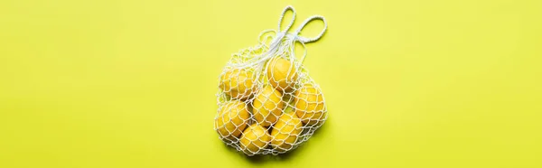 Top view of ripe whole lemons in string bag on yellow background, panoramic crop — Stock Photo