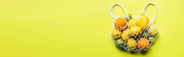 Top view of ripe whole citrus fruits in string bag on yellow background, panoramic crop — Stock Photo