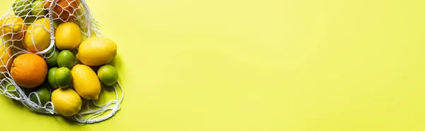 Top view of ripe whole citrus fruits in string bag on yellow background, panoramic crop — Stock Photo