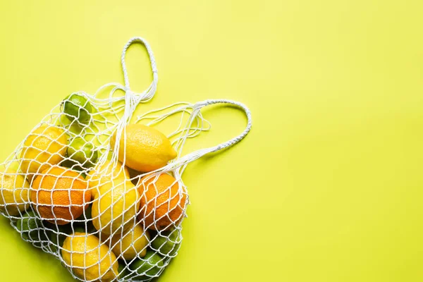 Top view of ripe whole citrus fruits in string bag on yellow background — Stock Photo