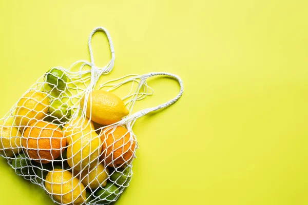 Vue du dessus d'agrumes entiers mûrs dans un sac à ficelle sur fond jaune — Photo de stock