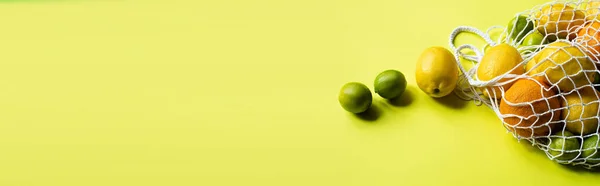 Ripe whole citrus fruits in string bag on yellow background, panoramic crop — Stock Photo