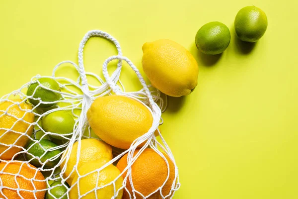 Ripe whole citrus fruits in string bag on yellow background — Stock Photo