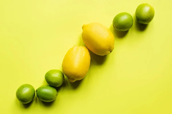 Vue de dessus des citrons mûrs et des citrons verts sur fond coloré — Photo de stock