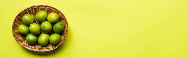 Top view of ripe limes in wicker basket on colorful background, panoramic crop — Stock Photo