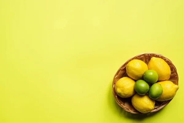 Верхний вид спелых лаймов и лимонов в плетеной корзине на красочном фоне — стоковое фото