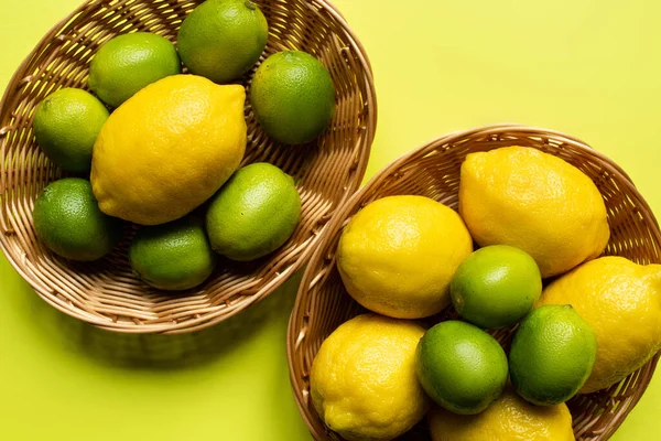 Vista superior de limas maduras y limones en cestas de mimbre sobre fondo colorido - foto de stock