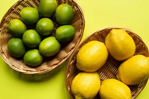 Vue de dessus des citrons et chaux mûrs dans des paniers en osier sur fond coloré — Photo de stock