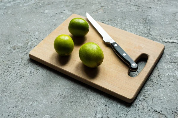 Limes mûres sur planche à découper en bois avec couteau sur surface texturée en béton — Photo de stock