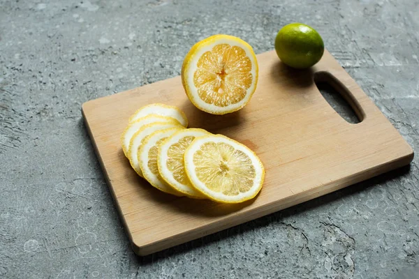 Limón y lima en rodajas amarillas maduras sobre tabla de cortar de madera sobre superficie texturizada de hormigón - foto de stock