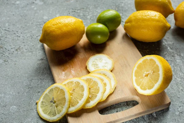 Citrons et citrons jaunes tranchés mûrs sur planche à découper en bois sur surface texturée en béton — Photo de stock