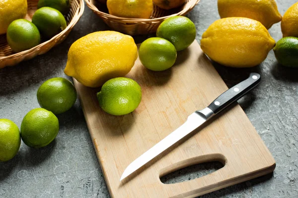 Ripe yellow lemons and limes on wooden cutting board with knife on concrete textured surface — Stock Photo