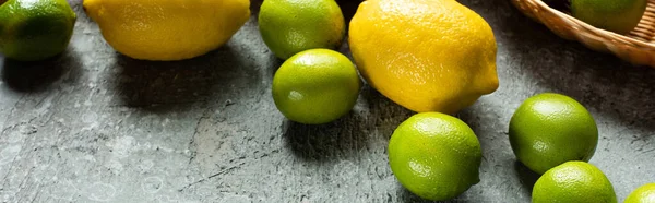 Limoni gialli maturi e limoni verdi su superficie testurizzata in calcestruzzo, coltura panoramica — Foto stock