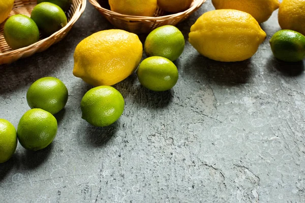 Ripe yellow lemons and green limes in wicker baskets on concrete textured surface — Stock Photo