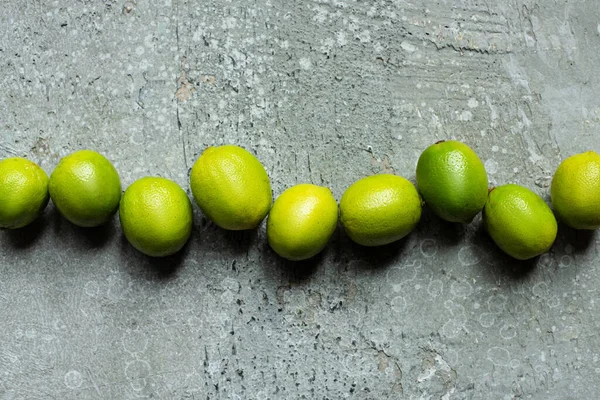 Vue de dessus des citrons verts mûrs sur la surface texturée du béton — Photo de stock