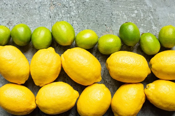 Vue de dessus des citrons jaunes mûrs et des citrons verts sur la surface texturée du béton — Photo de stock