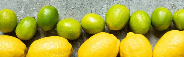 Vista dall'alto di limoni gialli maturi e limoni verdi su superficie testurizzata in cemento, coltura panoramica — Stock Photo