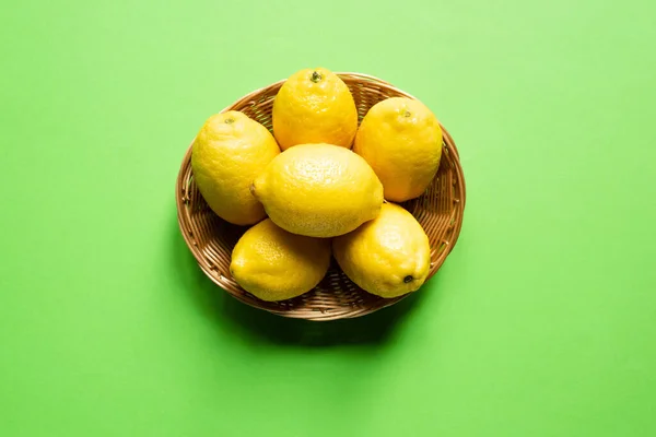 Ripe yellow lemons in wicker basket on green background — Stock Photo