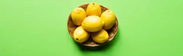 Ripe yellow lemons in wicker basket on green background, panoramic crop — Stock Photo