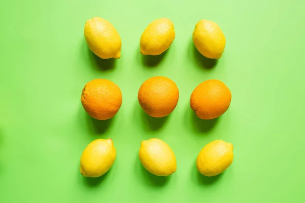 Flat lay com limões amarelos maduros e laranjas em fundo verde — Fotografia de Stock