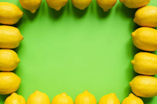 Vista superior de limões amarelos maduros dispostos em moldura no fundo verde com espaço de cópia — Fotografia de Stock