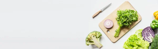 Vista superior de vegetais maduros perto de tábua de corte de madeira com salsa e cebola na superfície branca, tiro panorâmico — Fotografia de Stock