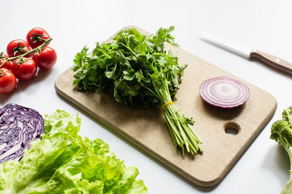 Surtido de verduras frescas y tabla de cortar de madera con cebolla roja y perejil sobre fondo blanco - foto de stock