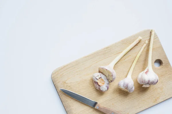 Top view of garlic on wooden chopping board with knife on white background — Stock Photo