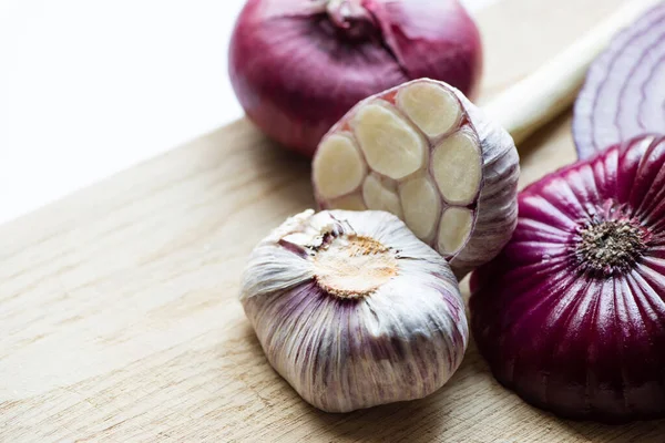 Nahaufnahme von roten Zwiebeln und Knoblauch auf einem Holzschneidebrett isoliert auf weiß — Stockfoto