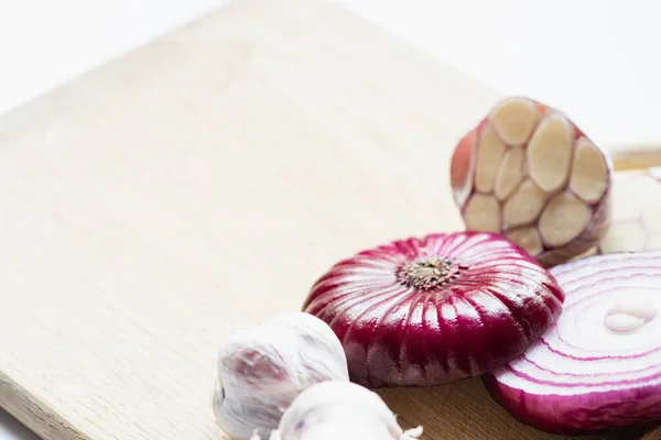 Nahaufnahme von roten Zwiebeln und Knoblauch auf einem Holzschneidebrett isoliert auf weiß — Stockfoto