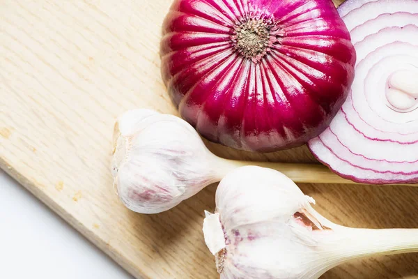 Draufsicht auf rote Zwiebel und Knoblauch auf Holzschneidebrett auf weißem Hintergrund — Stockfoto