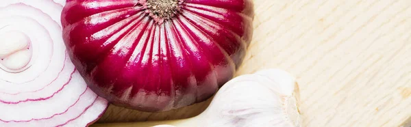 Close up view of red onion and garlic on wooden cutting board, panoramic shot — Stock Photo
