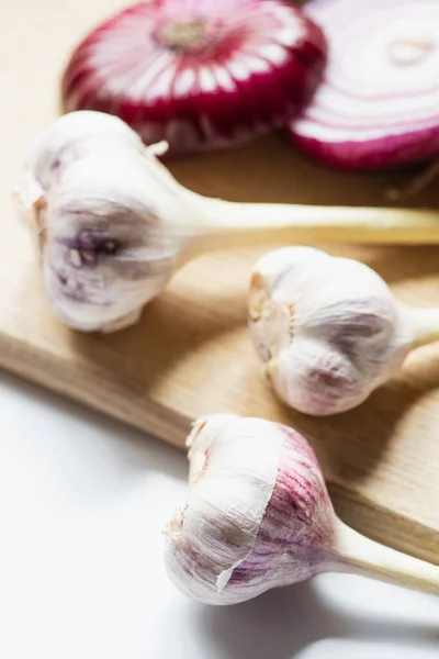 Selective focus of red onion and garlic on wooden cutting board on white background — Stock Photo