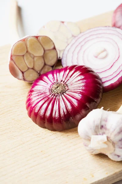 Close up view of red onion and garlic on wooden cutting board on white background — Stock Photo