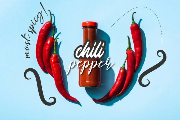 Top view of tomato sauce in bottle between chili pepper near most spicy lettering on blue — Stock Photo