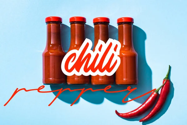 Top view of chill pepper lettering near tomato sauce in bottles on blue background — Stock Photo