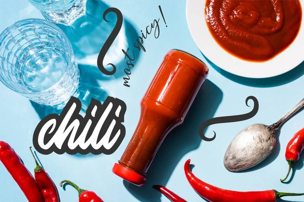 Top view of glasses with water, tomato sauce on plate and bottle beside chili peppers near most spicy lettering on blue — Stock Photo