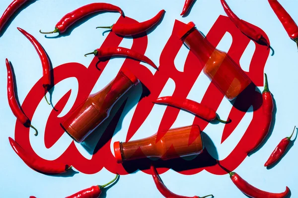 Top view of tomato sauce in bottles and ripe peppers near chili lettering on blue — Stock Photo