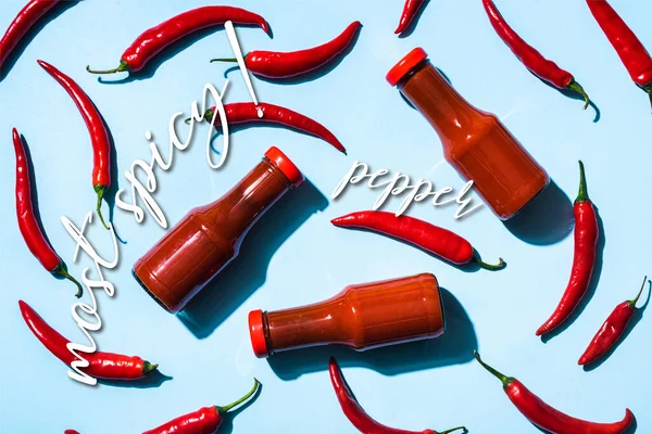 Draufsicht auf reife Chilischoten mit Tomatensauce in Flaschen in der Nähe der pikantesten Schriftzüge auf blau — Stockfoto