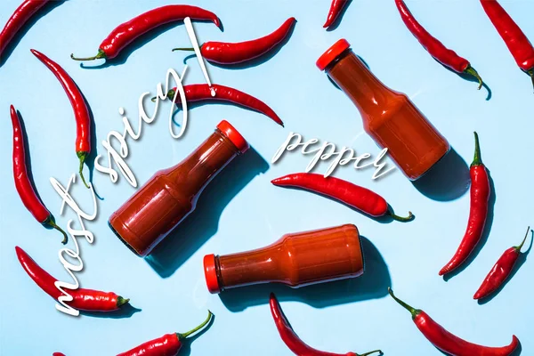 Vista superior de pimentas maduras com molho de tomate em garrafas perto de letras mais picantes em azul — Fotografia de Stock