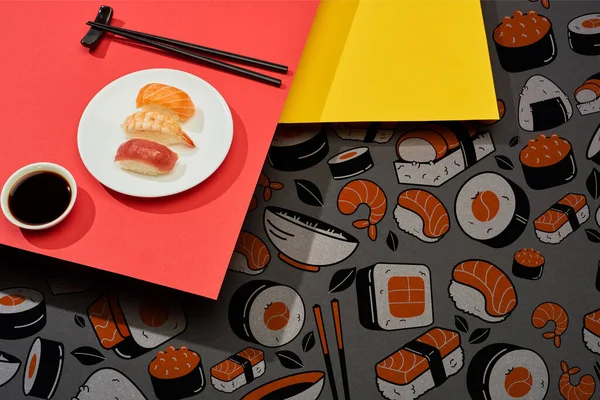 Fresh nigiri with salmon, shrimp and tuna near soy sauce, chopsticks and sushi illustration on red and yellow surface — Stock Photo