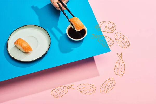 Cropped view of woman putting fresh nigiri with salmon into soy sauce near illustration on blue, pink background — Stock Photo
