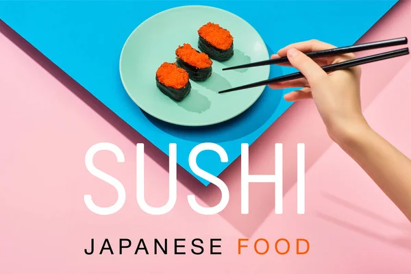 Vue recadrée de femme tenant des baguettes près de nigiri avec du caviar rouge et des sushis japonais lettrage alimentaire sur fond bleu, rose — Photo de stock