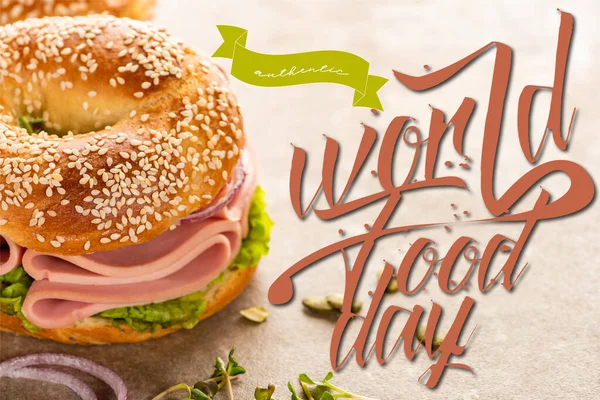 Fresh bagel with ham near world food day lettering on textured surface — Stock Photo