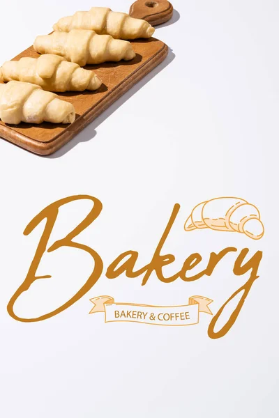 Rohe Croissants auf hölzernem Schneidebrett in der Nähe von Bäckereien und Kaffeebeschriftung auf weißem Hintergrund — Stockfoto