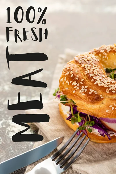 Tasty bagel with meat on napkin with cutlery near fresh meat lettering on textured surface — Stock Photo