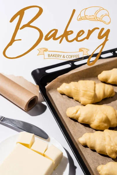 Selective focus of raw croissants on baking tray near butter, knife, bakery and coffee lettering on white — Stock Photo